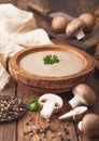 Wooden plate of creamy chestnut champignon mushroom soup with wooden spoon, pepper and kitchen cloth on wooden background Royalty Free Stock Photo