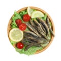 Wooden plate with delicious fried anchovies, lemon slices, tomatoes and lettuce leaves on white background, top view