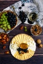 Wooden plate with different types of cheese, a basket with dark and green grapes, walnut, dates and a glass of white wine on a Royalty Free Stock Photo