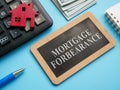 Wooden plate with inscription mortgage forbearance and model of house. Royalty Free Stock Photo