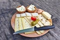 Wooden plate with a selection of cheeses, tomato, pickle and knife on a wooden table