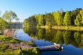 Wooden platform and calm water of the lake. The spring forest and the blue sky are reflected in the water.