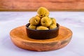 Wooden platter displaying an array of fresh green olives in a ceramic bowl.