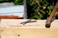 Wooden pole with a pile of nails and hammer in focus on a blurred rusty and nature background