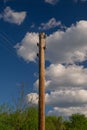 Wooden pole with a power line against a blue sky with clouds Royalty Free Stock Photo