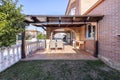 wooden porch of a single-family home with light brown stoneware floors, exposed brick walls, gardens with grass, trees and white Royalty Free Stock Photo