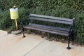 Wooden public bench with black wrought-iron sides and yellow trash can