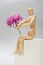 Wooden puppet with aster flower on cube on grey background