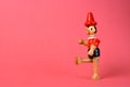 Wooden puppet depicting Pinocchio walking on a pink background