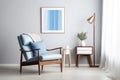 Wooden recliner chair with blue leather cushion near cabinet and side table against white wall with poster frame