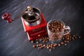 Wooden retro coffee grinder and transparent cup full of brown coffee beans and grains around on dark surface Royalty Free Stock Photo