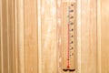 Wooden retro-style thermometer on a wall of yellow planks with a scale in degrees Celsius and a red mark on a hundred in the