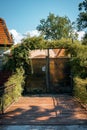 Wooden road with metal fences on sides leading to a mesh gate with plant arch