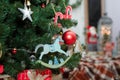 wooden rocking horse toy and decorations hanging on fir tree branches with santa claus and lantern lights on blurry background. Royalty Free Stock Photo