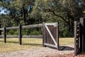 Wooden rural fence with open gate in sunshine with trees in background