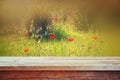 Wooden rustic table in front of red poppies against sky with light burst. vintage filtered image. product display