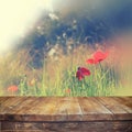 Wooden rustic table in front of red poppies against sky with light burst. vintage filtered image. product display