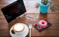 Wooden rustic table with a warm homemade cappuccino and a pink donut with some fruit. Good morning breakfast. Tablet to stay