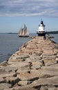 Sailboat Passes by Lighthouse on Edge of Breakwater in Maine