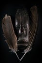 Wooden sculpture of human face in African style with big feathers around it. Dark wood carving. African tribal mask Royalty Free Stock Photo