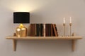 Wooden shelf with different books, burning candles and lamp on light wall Royalty Free Stock Photo