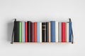 Wooden shelf with many hardcover books on white wall