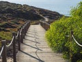 wooden sidewalk leading to Praia da Baia da Arquinha beach with ocean sand dunes footpath and green bush and vegetation