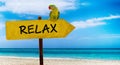Wooden sign on beautiful beach and clear sea wit text relax. A green parrot sits on a pointer to a tropical paradise Royalty Free Stock Photo