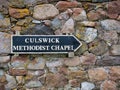 A wooden sign on a colourful, old stone wall points the way to the small, remote Methodist Chapel at Culswick, Mainland, Shetland