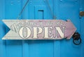 Wooden sign hanging by a chain saying `Yes!Come in we are open` against a blue door background. Royalty Free Stock Photo