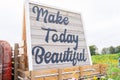 Wooden sign on tractor that says Make Today Beautiful in cursive writing in a flower field