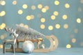 Wooden sleigh with small fir tree near decorative reindeer and Christmas ornament on light blue table against blurred lights. Royalty Free Stock Photo