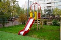 A wooden slide of bright red and yellow color against the background of green trees and residential buildings Royalty Free Stock Photo