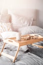 Wooden small breakfast table stands on bed in bedroom, gray sheets, sun shines through window sunrise