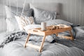 Wooden small breakfast table stands on bed in bedroom, gray sheets, sun shines through window sunrise