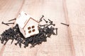 a wooden small house with a window stands on a pile of black screws, a house on nails Royalty Free Stock Photo