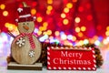 Wooden snowman figurine and Merry Christmas sign. Christmas composition on blurred lights background Royalty Free Stock Photo