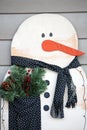 A wooden snowman winter decoration with a cloth scarf and pocket filled with winter greens, pinecones and berries