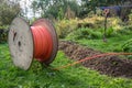 Wooden spool with fiber optic cable for fast internet ready to be laid in narrow trenches in the ground on a meadow,