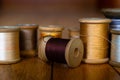 Cream, Grey, Yellow, Dark Grey, Gold, White, and Silver Thread on Wooden Spools Sit on a Series of Wooden Planks