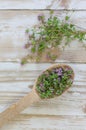 Wooden spoon with blooming thyme on a white wooden table top view