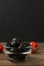 Closeup of glass bowl of black olives, red tomatoes on the wooden board against dark wall Royalty Free Stock Photo