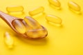 Wooden spoon with Omega 3 pills on yellow background. Supplement food vitamin D capsules. Close up