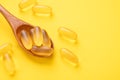 Wooden spoon with Omega 3 pills on yellow background. Supplement food vitamin D capsules. Top view. Copy space