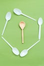 Wooden spoon with plastic alternatives on green background. Vertical. Organic concept