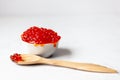 A wooden spoon is placed next to a white cup full of red caviar Royalty Free Stock Photo