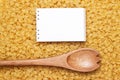 Wooden spoon on uncooked macaroni and notebook