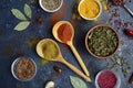 Wooden spoons with yellow and orange spices, different cups with dried herbs, garlic, bay leaf on a dark blue background