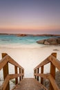 Wooden staircase leading down to a beach at dusk with orange granite rocks in the water and soft color in the sky caused by bush Royalty Free Stock Photo