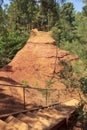 Wooden stairs on the hiking trail in Sentier des Ocres in France, a natural orange ocher path surrounded by a green forest Royalty Free Stock Photo